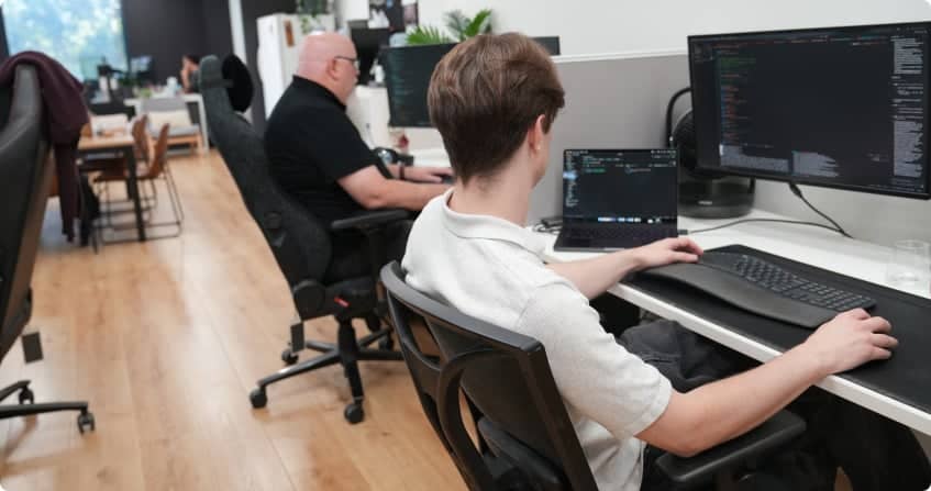 click click media and paladine systems developers working at their desks in the norwest sydney office on vibe code rescue projects with code visible on dual monitors.