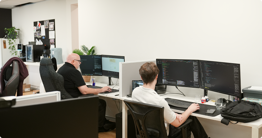 two paladine systems developers working at adjacent multi-monitor workstations with code open across their screens in the click click media norwest office.