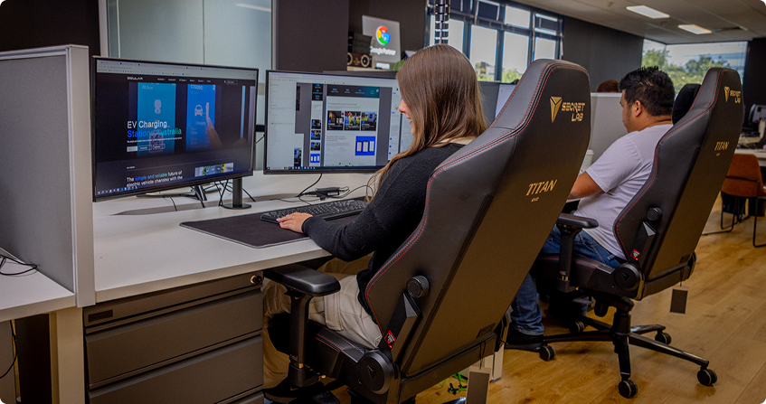 a click click media team member working at a multi-monitor desk in the norwest office with a website build open on screen, while a colleague works at the next workstation.