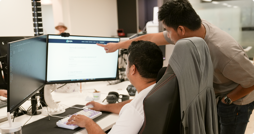 two click click media team members at a dual-monitor workstation reviewing a website terms and conditions page, with one pointing at the screen while the other navigates from the keyboard.